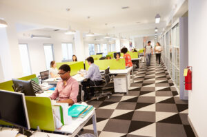 Modern office space with workers brightly lit with a wall of windows.