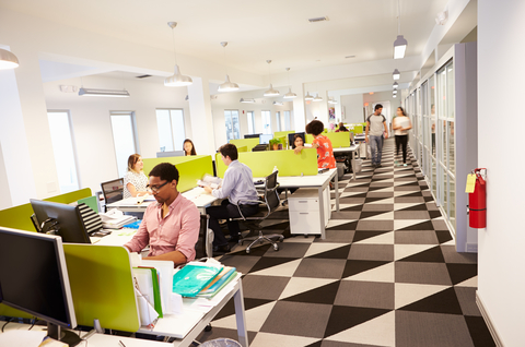 Modern office space with workers brightly lit with a wall of windows.